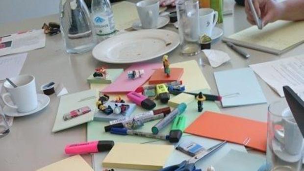 verschiedene Stifte, post-it, eine Schere und mehrere Playmobilfiguren liegen auf einem Tisch.